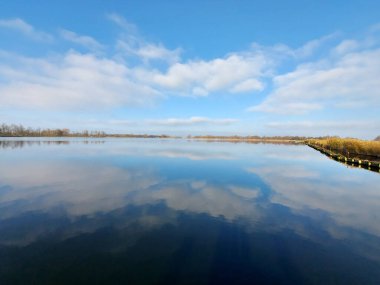 Gök mavisi gökyüzünde beyaz bulutlar Hollanda 'nın Zevenhuizen şehrindeki Rottemeren' in su yüzeyinde yansıyor.