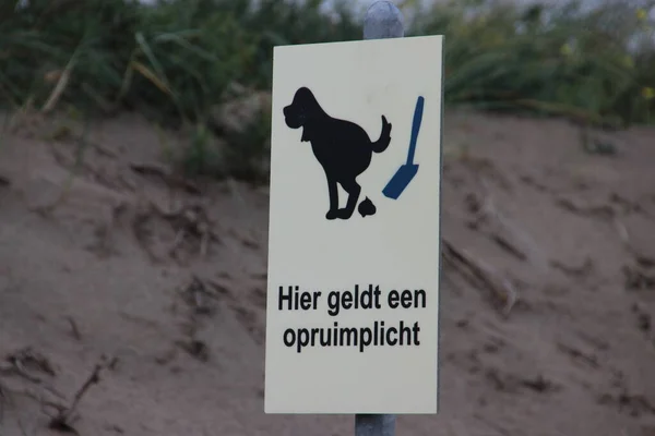 Sign with here is an obligation to clear in the Dutch language. Dog owners must clean up the excrement in Noordwijk