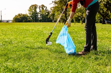 Parkta plastik ve kağıt toplayan insanlar. Sarı eldivenli gönüllü kadın ve parkta temizlik için çöp toplayan. Ekoloji kavramı
