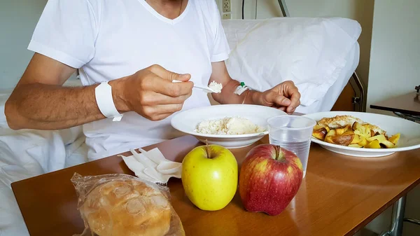 Male patient in hospital bed eating rice, fish with potatoes and apple. Hospital dish and healthy diet concept.