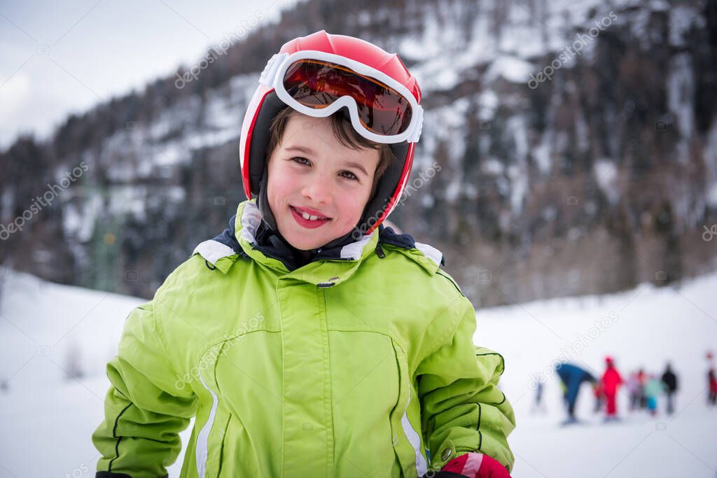 Portrait of happy child skier preparing to ride downhill steep slope. Active child with safety helmet and goggles. Winter sports concept. 