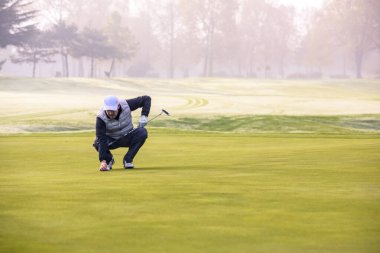 Golf oyuncusunun yakın plan fotoğrafı. Golf topunu yeşilde cebine atıyor.