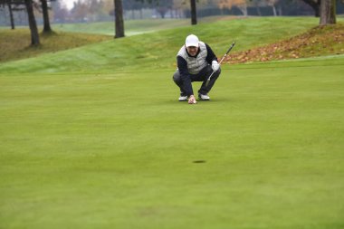 Golf oyuncusunun yakın plan fotoğrafı. Golf topunu yeşilde cebine atıyor.