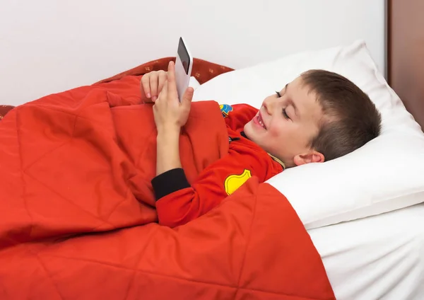 Child under the covers in bed looks at cellphone before falling asleep.