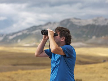 Bir dağın tepesinde duran ve uzaktan dürbüne bakan bir adamın portresi, Campo Imperatore, Gran Sasso Ulusal Parkı, Abruzzo bölgesi, İtalya. Seyahat konsepti. Geleceğe bakan insan kavramı. 