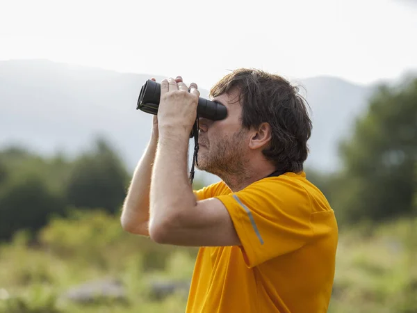 The hiker does bird watching with binoculars in the mountain nature park in search of birds of prey. Man scans the sky with binoculars. Concept of person looking to the future.