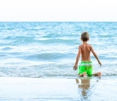 Mayo giymiş bir çocuk güneşli bir günde kumsalda oynar..