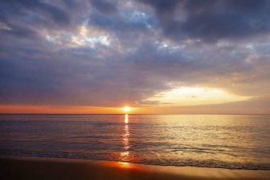 Deniz kabuğunun üzerinde bulutlu arka planda güzel bir gün batımı. Tropik sahilde gün batımı. Doğal yaz konsepti. Sarı ışıkla günbatımının zirvesi deniz suyunu yansıtır. Huzurlu deniz manzarası. Suyun üzerinde ufuk..