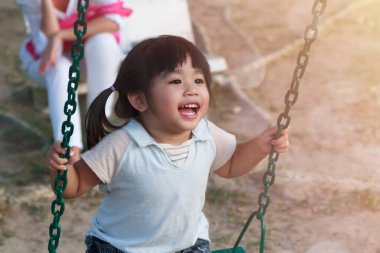 Küçük tatlı bir kız oyun sahasında salıncakta salıncak oynuyor. Sıcak ve güneşli bir günde. Asyalı kızlar oyun alanında salıncakta sallanmaktan mutlu olurlar.