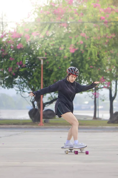 Asian women on skates board outdoors on beautiful summer day. Happy young women play surfskate at park on morning time. Sport activity lifestyle concept