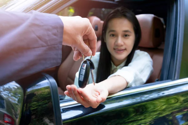 Close up of dealer giving key to new owner car. New car. Auto dealer giving woman automobile key for test drive on country road. Soft focus  smiling women try to test drive a car on road with dealer.