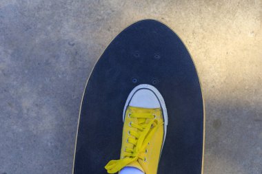 Üstteki manzarayı kapat Sarı spor ayakkabılar parktaki sörf tahtasına basıyor. 