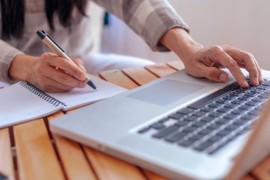 Genç iş kadınlarının ellerini kağıda not yazarak kapat. Kadın yönetici ofis masasında oturuyor. Tahta masaya yerleştirilmiş spiral not defterine yazı yazan bir kadın eli.