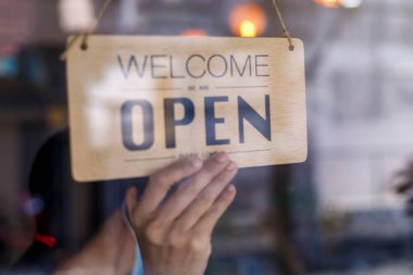 Asyalı perakendecinin eli, kafeteryadaki kadının tabela açması. Koronavirüs salgınına karşı koruma. Covid-19 karantinası nedeniyle açık dükkan, restoran veya bar.