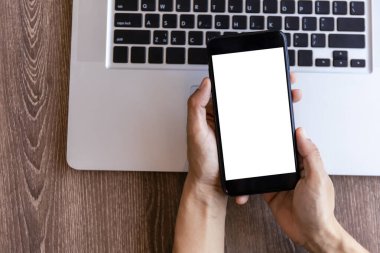 Üst görüşlü kadın elleri beyaz ekranlı akıllı telefonu tutuyor. Kadınlar çalışma alanına el uzatıyor, ahşap masa zemininde metin ve içerik için akıllı telefonu boş ekranla tutuyor.