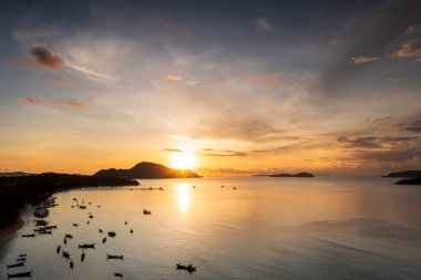 Bir sürü uzun kuyruklu tekneyle gündoğumunun tropikal sahildeki hava aracı görüntüsü. Sabahın erken saatlerinde sakin deniz ve gökyüzü üzerinde uzun kuyruklu teknelerle