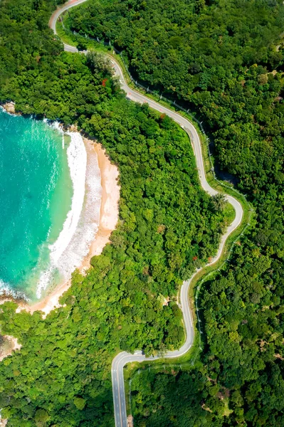 Aerial drone top down view of waves breaking in the sand with road and forest. High angle view of tropical sea with Seafront road.