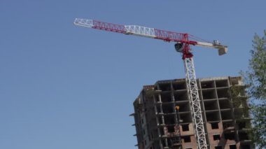 Mavi gökyüzü arka planında bir inşaat vinci. Kırmızı ve beyaz bir vinç bir bina inşa ediyor. İnşaat devam ediyor..
