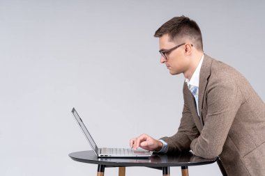 Masasında dizüstü bilgisayarı olan bir iş adamı. Takım elbiseli adam gri arka planda izole edilmiş..