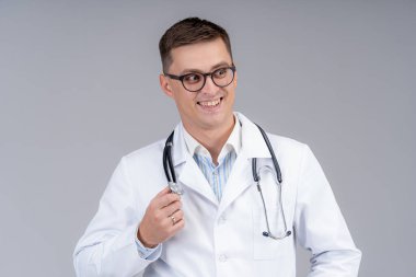 Önlüklü doktor portresi. Gri arka plan. Fonendoskopla gülümseyen gözlüklü doktor. Yakın çekim..