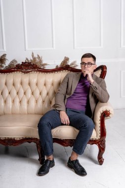 İç mekanda poz veren yakışıklı bir adamın portresi. Erkek, açık kahverengi lüks koltukta oturuyor..