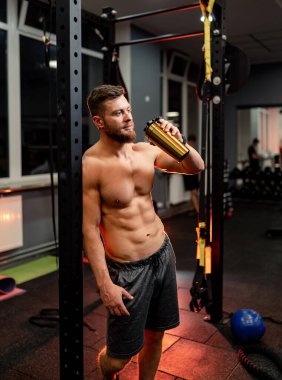 Vücut geliştirici ağır eğitimden sonra demir engelinin yanında duruyor. Çıplak gövde ve mükemmel karın kasları..