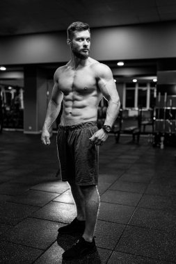 Kaslı yakışıklı bir adam, spor salonundaki kameraya poz veriyor, siyah beyaz bir fotoğraf. Gülümseyen bir vücut geliştiricinin portresi. Yakın çekim..