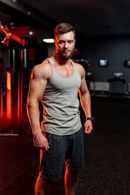 Atletik adam kameraya bakıyor. Büyük kaslar, güçlü kaslar. Jimnastik arka planında yakışıklı bir model..