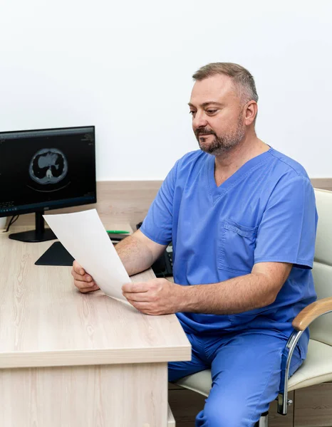 Portrait of a doctor or medical specialist. Vertical portrait. Man in scrubs sitting at table with papers in hands.