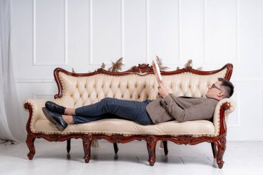 Genç işadamı şık bir kanepede dinleniyor. Adam kanepede yatarken dergi okuyor..