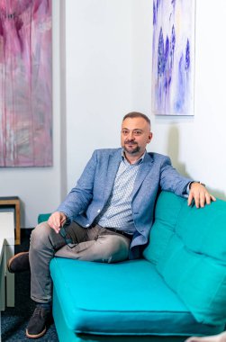 Büyük, mavi bir kanepede rahatlayan mutlu ve memnun bir iş adamının görüntüsü. Modern iç arkaplan.