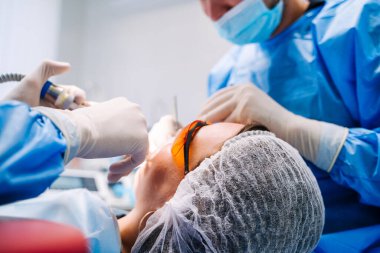 Dişçiler stomatolojiyi kontrol ederler ve güvenlik gözlüklü genç bayan hastaların dişlerini onarırlar. Yandan bak. Sağlıklı diş konsepti