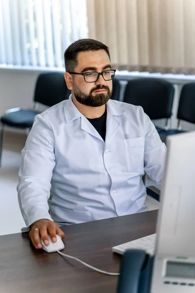 Doctor in scrubs working on the computer. Sitting in chair in medical office.