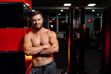 Sporcu spor salonundaki kolona yaslanarak el ele tutuşuyor. Mükemmel vücudu ve güzel gülüşü olan gömleksiz yakışıklı bir adam..