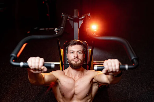 Handsome young man doing bench press workout in gym. Orange warm light. Strong abs. Heavy lift.