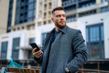 Ofis geçmişinde yakışıklı genç bir iş adamı. Telefon ellerinde. Yakın çekim..