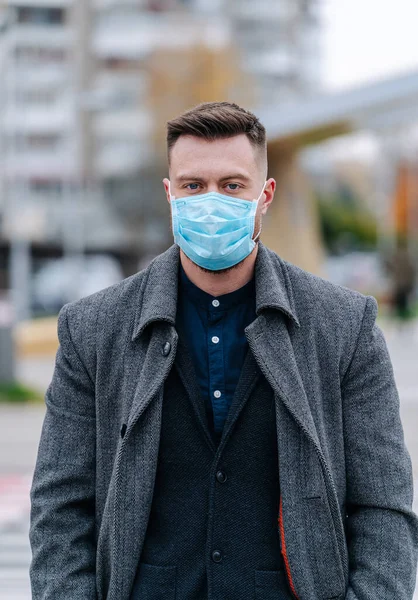 Handsome young man in coat and suit on the street with a medical face mask on. Protection against infection. Influenza virus or coronavirus.