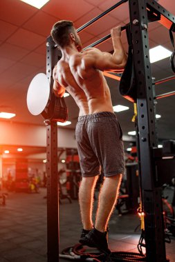 Yatay çizgide, spor salonunun arka planında, gömleksiz, yakışıklı, güçlü bir adamın portresi. Erkek güzellik konsepti. Arkadan bak. Yakın çekim..
