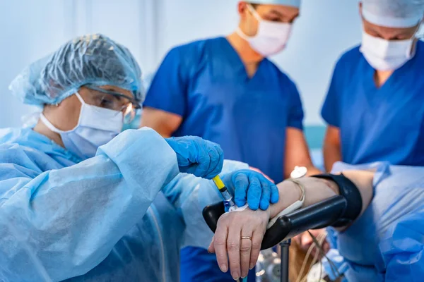 Hand of a patient lying on the operating table. Pulse oximeter sensor on the finger. The patient is sleeping under general anesthesia. Doctors near patient.