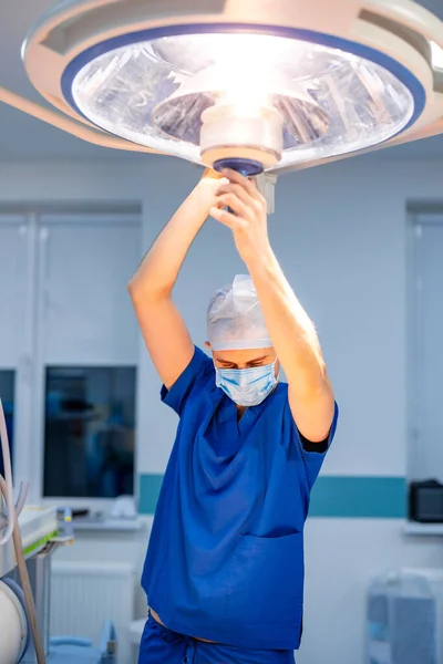 Surgical lamp in operating room, intended to assist medical personnel during a surgical procedure. Doctor fixes lamp for illuminating a local area or cavity of the patient.