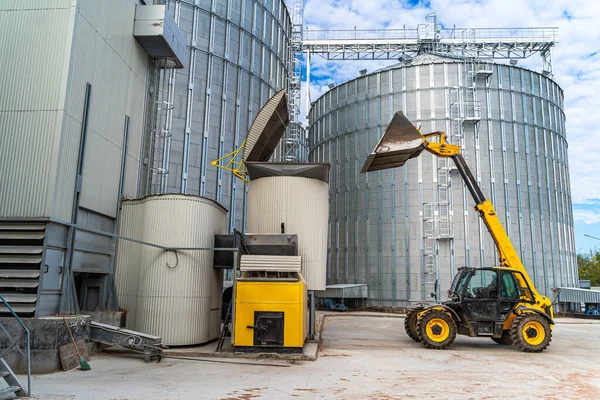 Agricultural silo, foreground sunflower plantations. Building exterior. Storage and drying of grains, wheat, corn, soy, sunflower against the blue sky with white clouds.