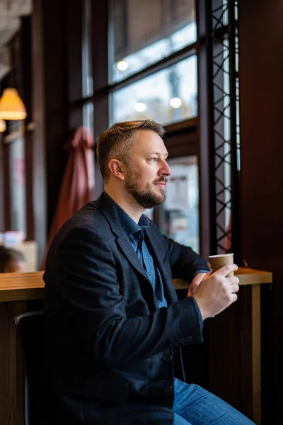 Authentic image of a pensive businessman in a coffee shop. Businessman in dark jacket having break.