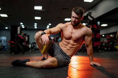 Çok kaslı bir sporcu, koyu kırmızı arka planda çıplak gövde ile protein içiyor. Atletik vücut. Spor ve spor beslenme konsepti.