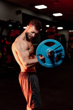 Gömleksiz genç vücut geliştirici eller için egzersiz yapıyor. Güçlü karın kasları. Karanlık ışık. Fotoğraf yan taraftan..