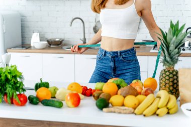 Mutfakta santimetre boyunda mutlu bir kadın. Masada taze meyve ve sebze var. Sağlıklı beslenme.