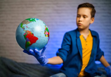 Çocuk küreye bakıyor. Dünya gezegeninin modeli. Çocuk virüse dikkat et. Salgın. Coronavirus. COVID-19