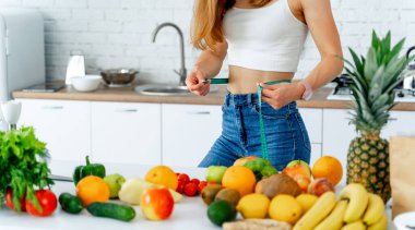 Mutfakta santimetre boyunda mutlu bir kadın. Masada taze meyve ve sebze var. Sağlıklı beslenme.