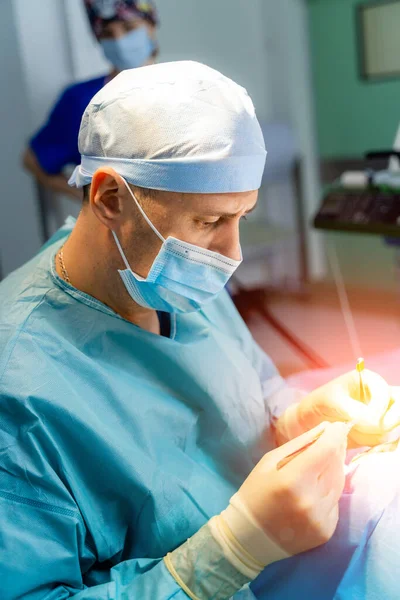 Plastic surgeon performs cosmetic surgery in hospital operating room. Surgeon in mask performs medical procedure. Breast augmentation, enlargement, enhancement.