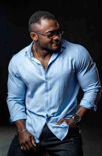 Fashion studio portrait of young african american handsome man. Male in light shirt poses to the camera on black background.