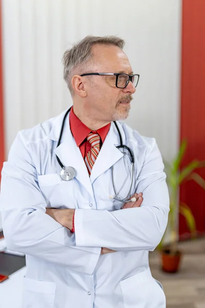 Portrait of a senior male doctor sitting at doctor\'s office and looking at side. Thoughtful face of experienced doctor.